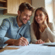 Jeune couple souriant à la cuisine avec documents et ordinateur